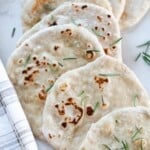 sourdough flat bread topped with fresh rosemary layered in a line on a white quartz countertop with a plaid towel to the left