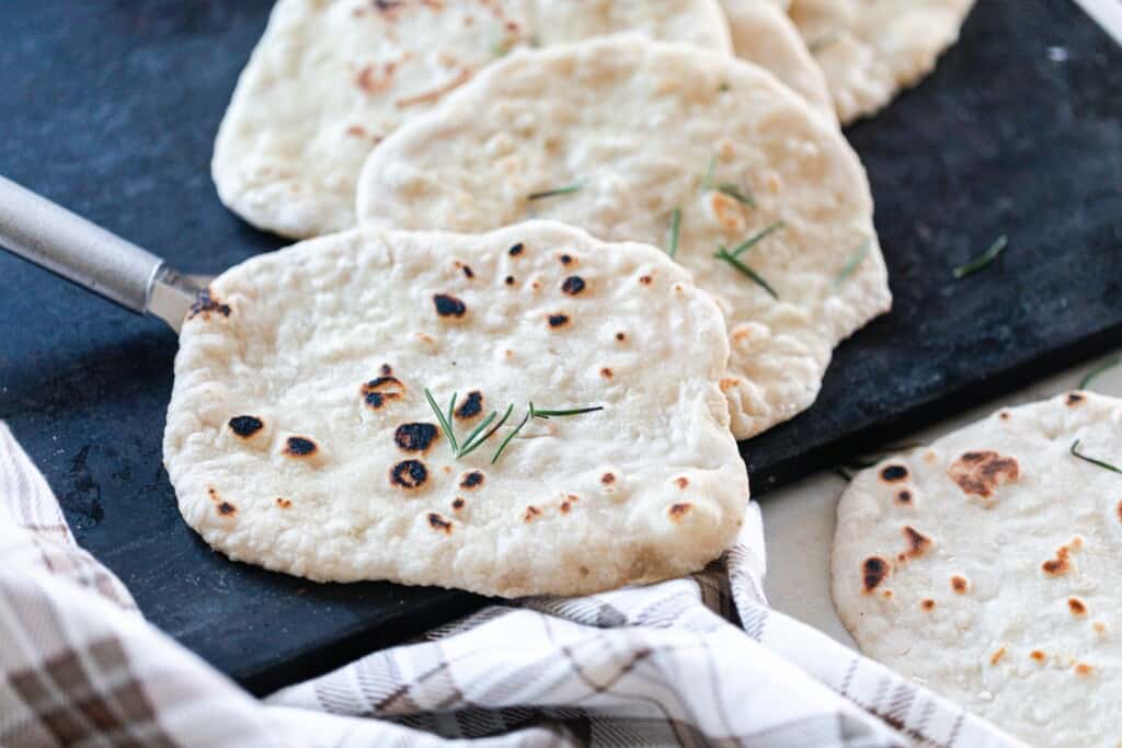 sourdough flatbreads placed on a black serving tray with a plaid towel in the front