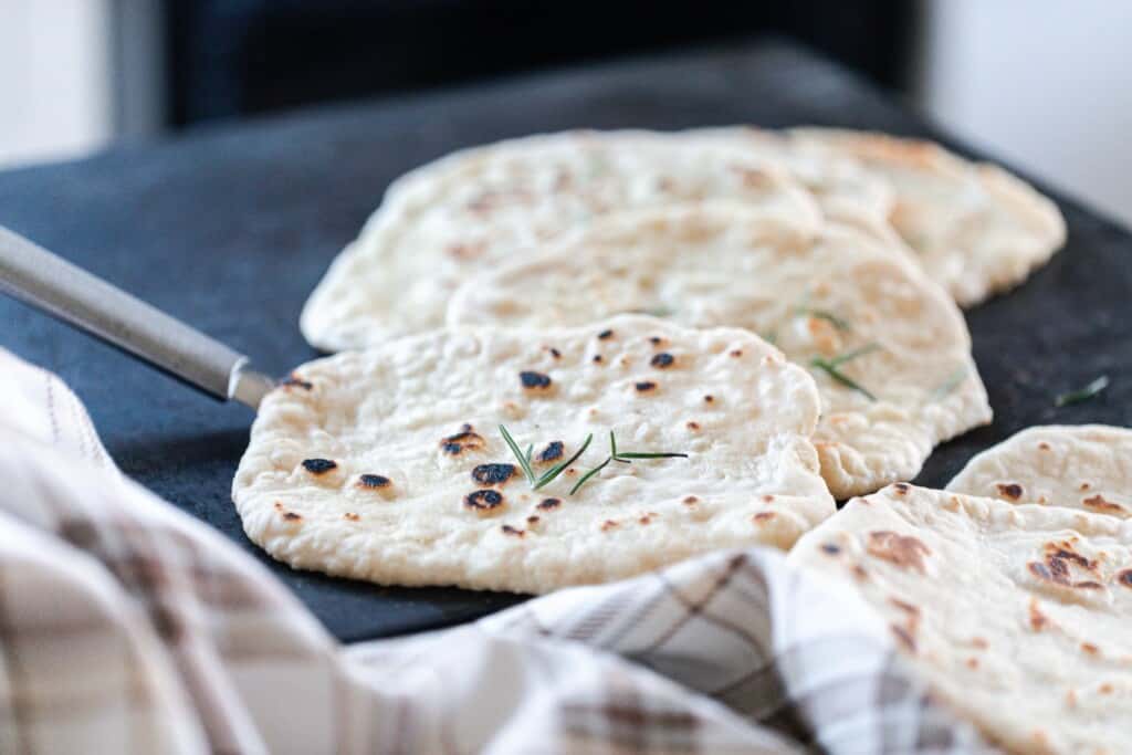 sourdough flatbreads layered on a black serving tray with a plaid towel in the front