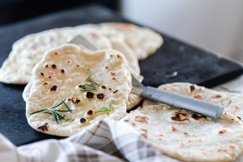 sourdough flatbread being lifted up by a spatular with more flatbreads on a black serving tray in the background