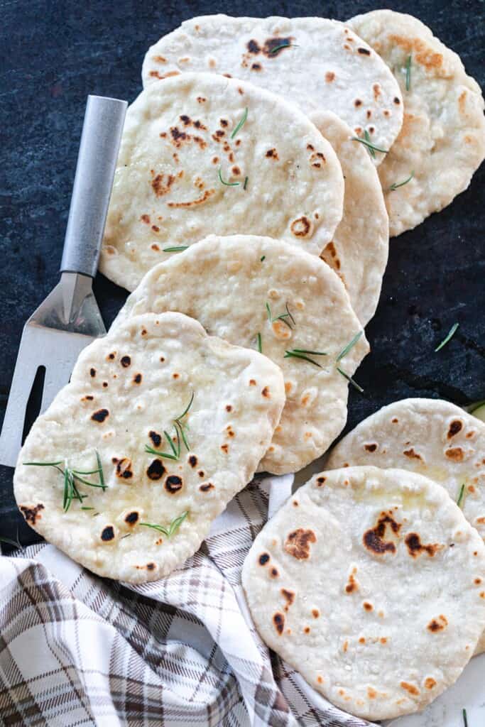 overhead photo of lots of sourdough flatbread on a black serving tray with a stainless steel spatula to the right of the flatbreads