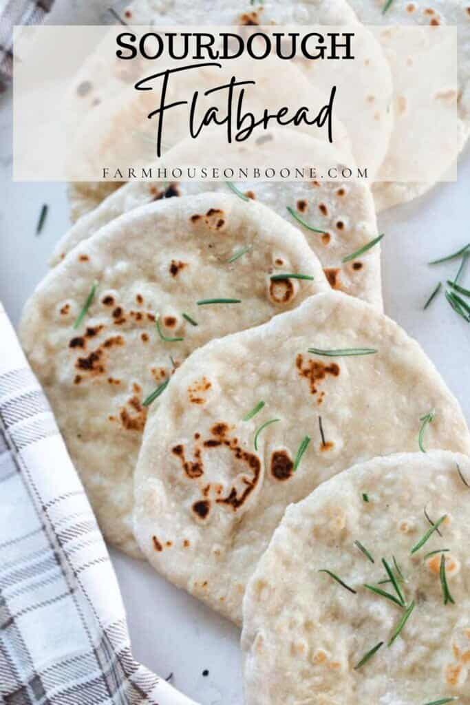 sourdough flat bread topped with fresh rosemary layered in a line on a white quartz countertop with a plaid towel to the left