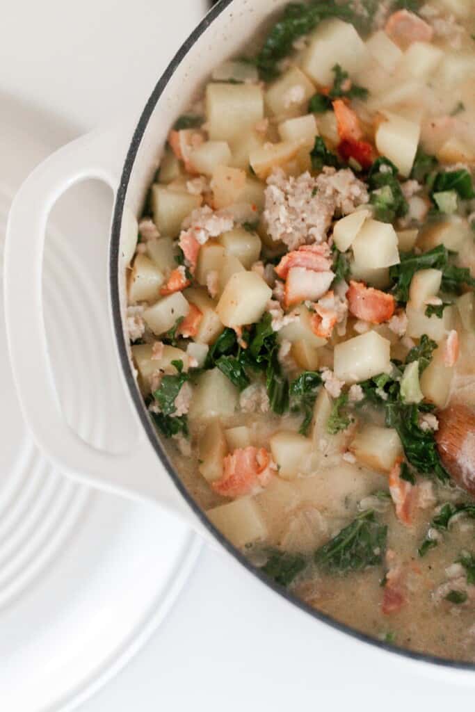 overhead photo of a dutch oven full of creamy soup with potatoes, bacon, kale, sausage