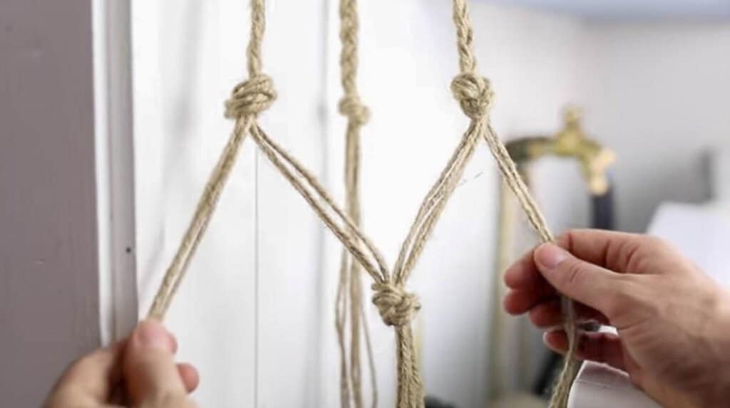 hands holding out jute strings that are knotted in different spots creating somewhat of a net.