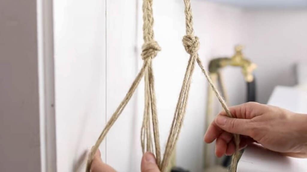 a hand holding four strands of jute string separating some strands while combining others