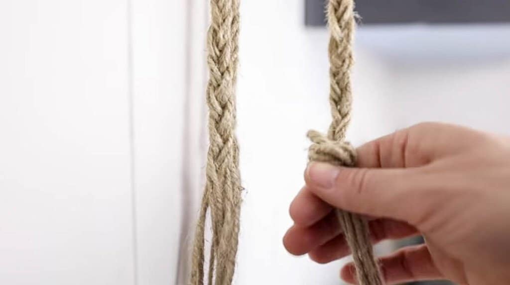 hand adding a knot to the bottom of a braid made from jute