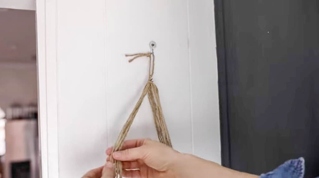 jute string folded in half and held together by a string wrapped around them and hung up with a nail on a wall.