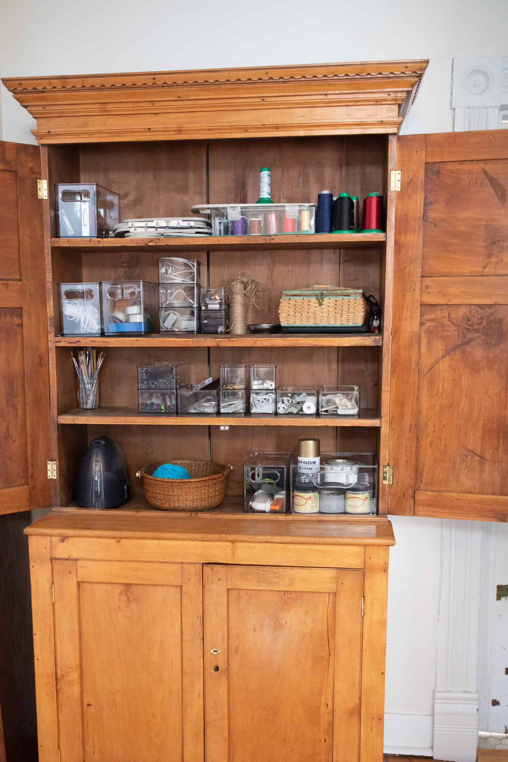 an organized antique wooden cabinet storing craft and sewing items in baskets, jars, and clear bins