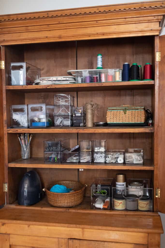 A close up picture of a craft cabinet organized with clear containers and vintage baskets