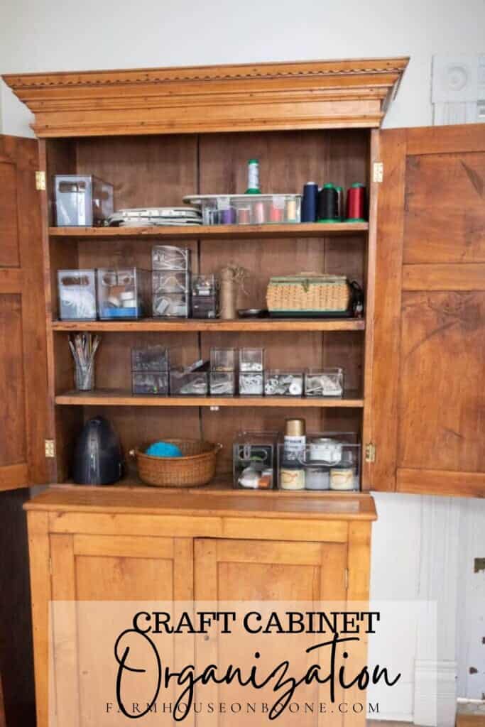 an organized antique wooden cabinet storing craft and sewing items in baskets, jars, and clear bins