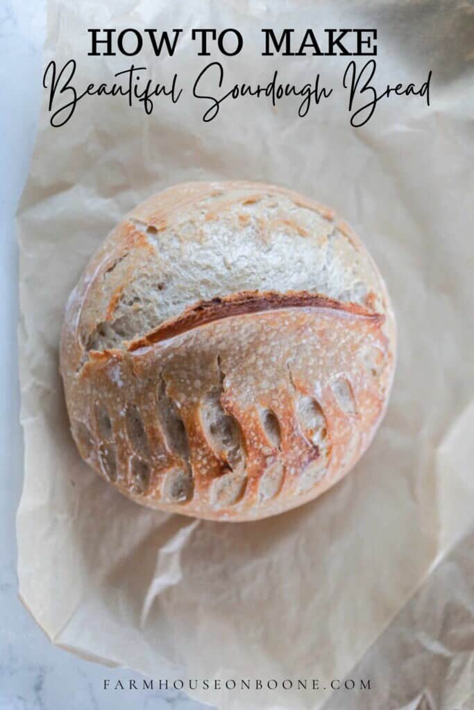 overhead photo of a loaf of sourdough bread with a wheat and half moon shaped pattern in it on parchment paper