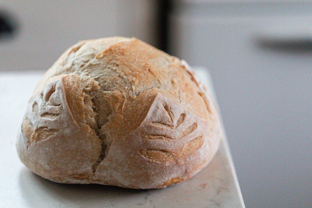 loaf of sourdough bread with a cross score and wheat pattern down the sides