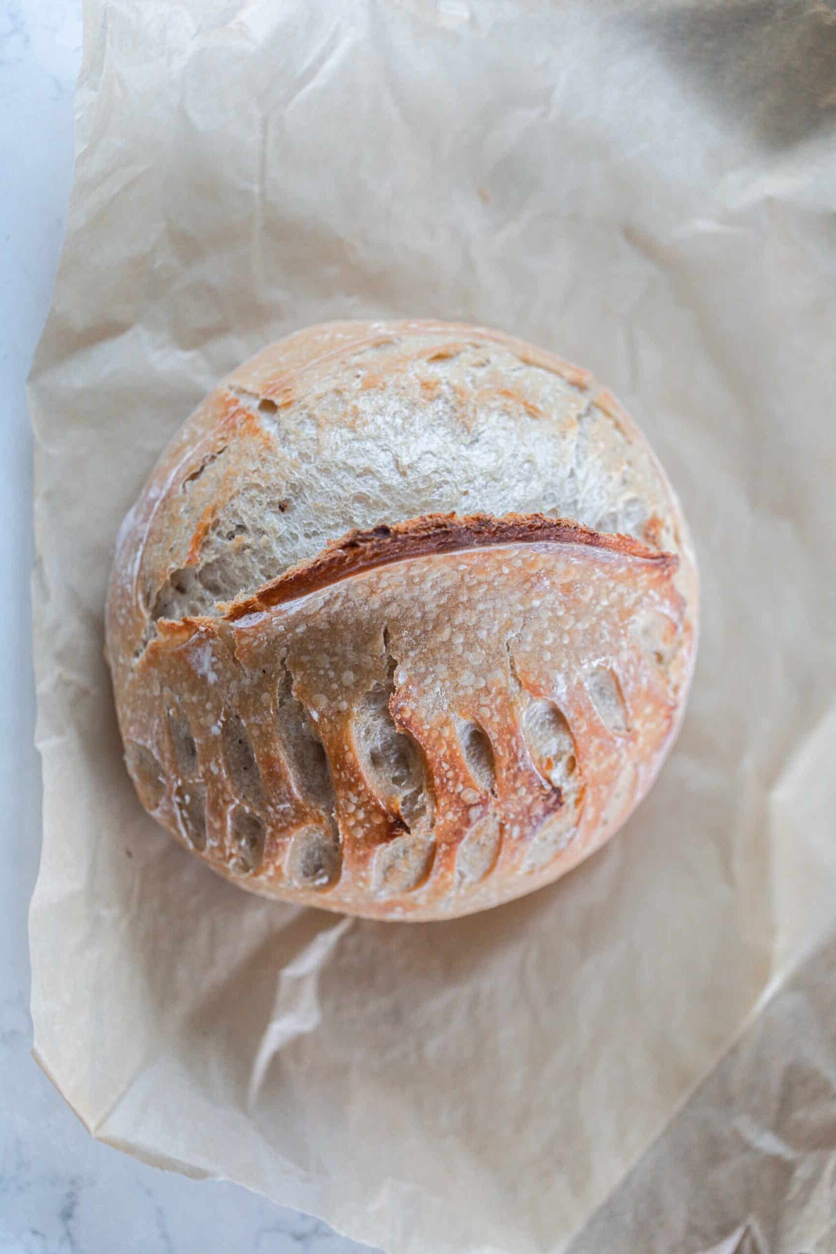 overhead photo of a loaf of sourdough bread with a wheat and half moon shaped pattern in it on parchment paper