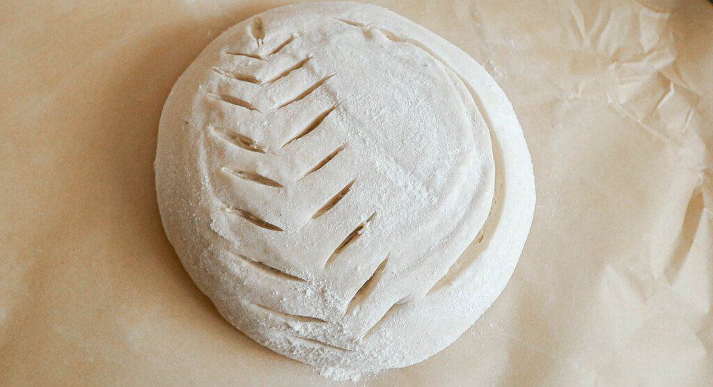 sourdough bread dough scored with a wheat pattern and half moon shape on  parchment paper ready for the oven 