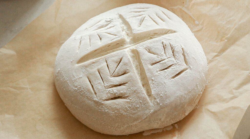 sourdough bread dough scored with a cross in the middle and wheat pattern on the side