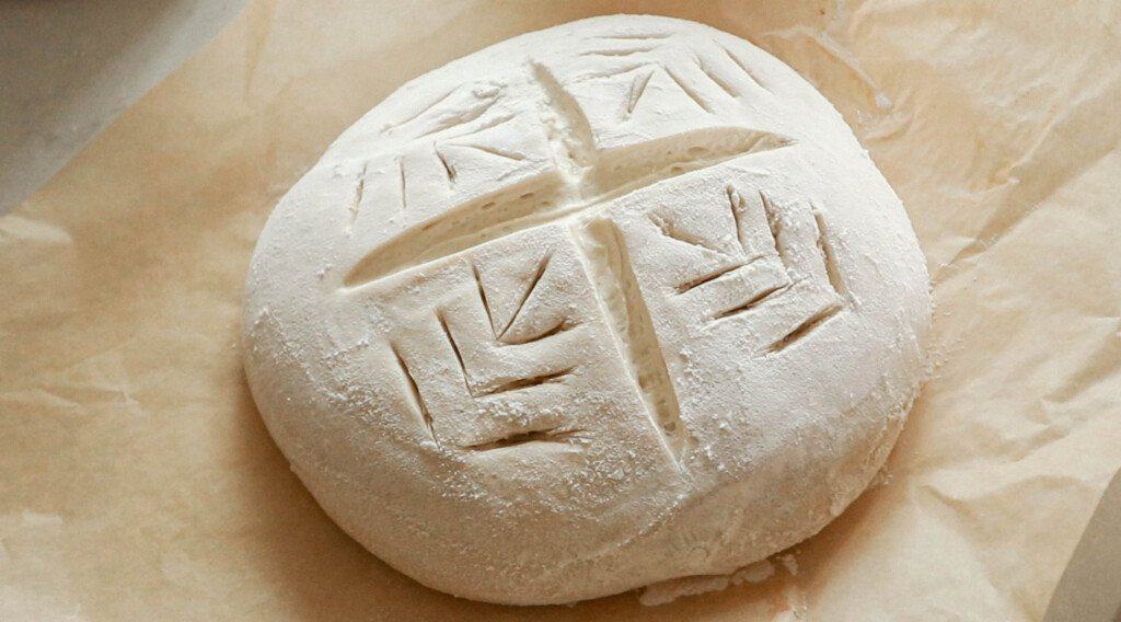 sourdough bread dough scored with a cross in the middle and wheat pattern on the side