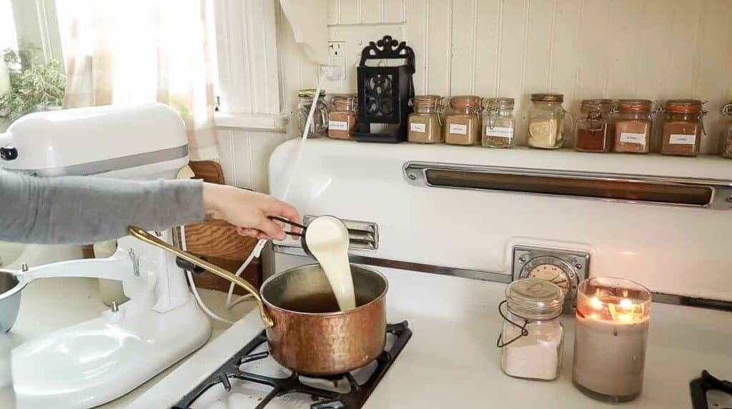 cream being poured into a copper pot on a white vintage stove to make cream cheese icing