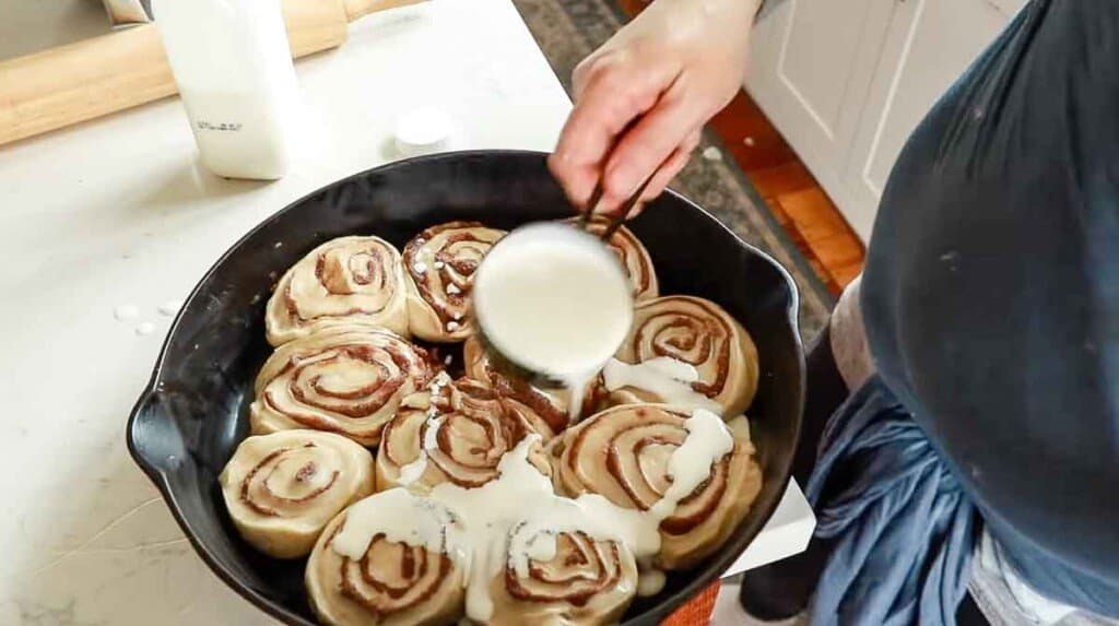 cream being poured over unbaked sourdough cinnamon rolls in a cast iron skillet