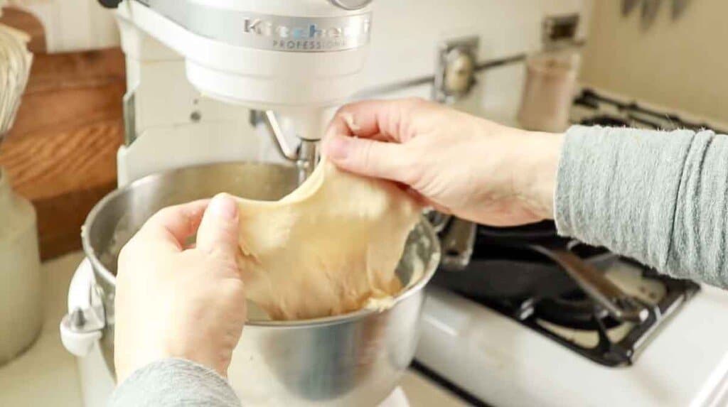 hands pulling sourdough dough apart to do the windowpane test