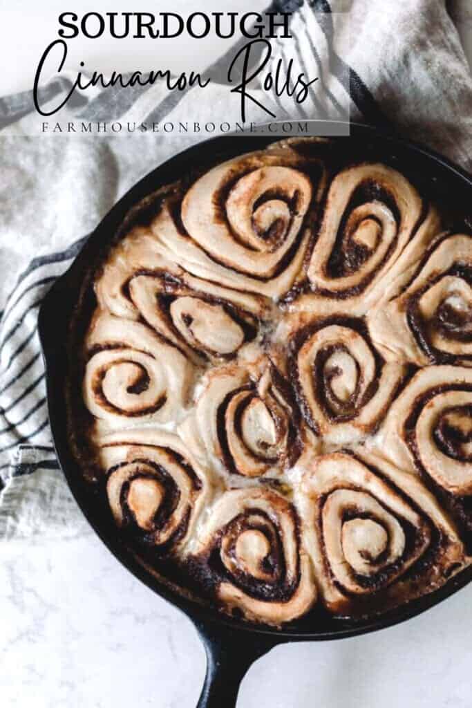 overhead photo of sourdough cinnamon rolls in a cast iron skillet on a white and black stripped towel on a white quartz countertop