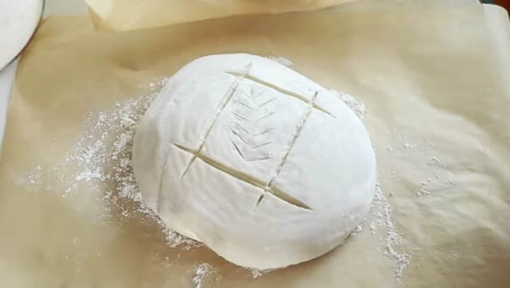 sourdough scoring design with a loaf of bread with a square scored with a wheat pattern in the center of the square. The loaf is on parchment paper