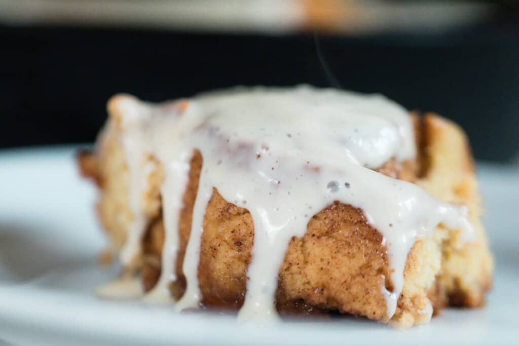 creamy cream cheese frosting glazed over a cinnamon roll made with einkorn flour on a white plate