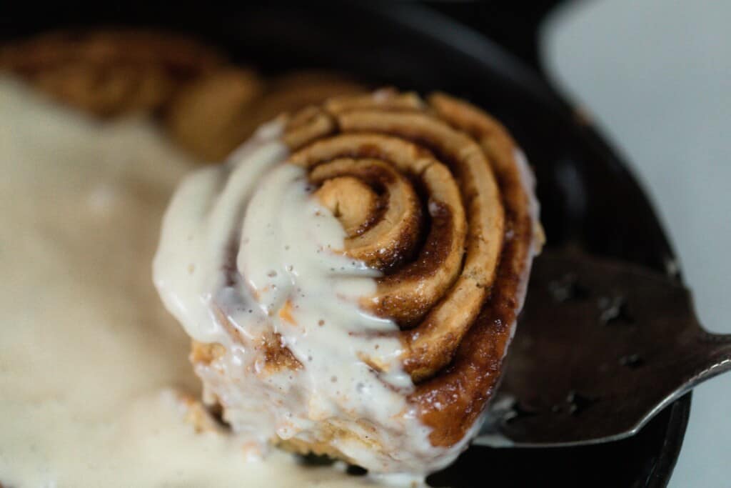 a einkorn cinnamon roll topped with cream cheese frosting being picked up with a spatula