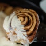 a einkorn cinnamon roll topped with cream cheese frosting being picked up with a spatula
