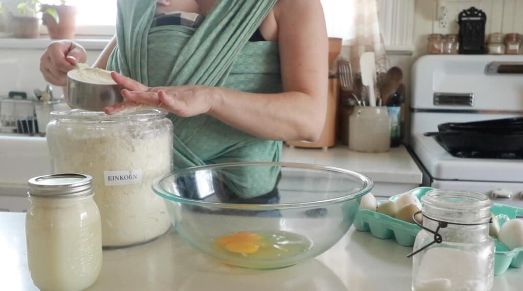 einkorn flour being measured and leveled with hand about to be added to a glass bowl with eggs.