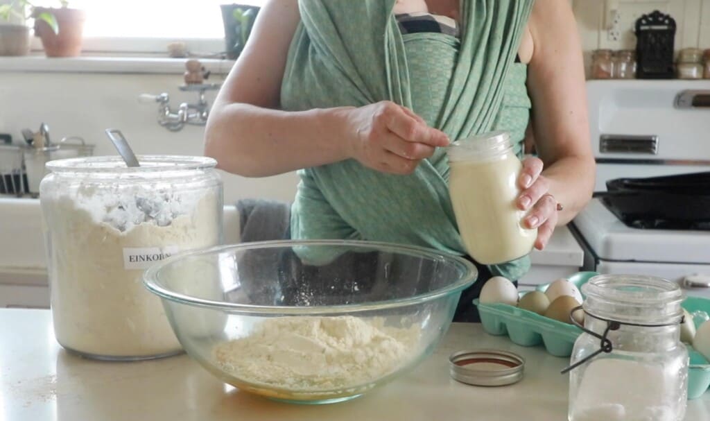 fresh milk in a mason jar being measured into a tablespoon to pour into a glass bowl with flour and eggs.