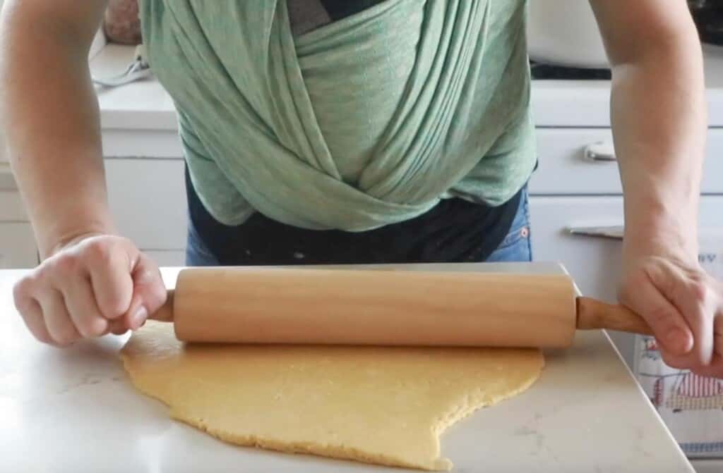 rolling out homemade noodle dough for soup on a white countertop with a rolling pin