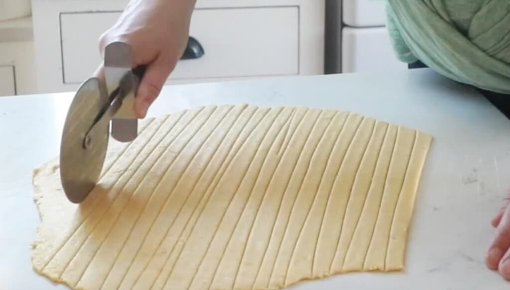 homemade egg noodle dough sliced into strips on a white countertop