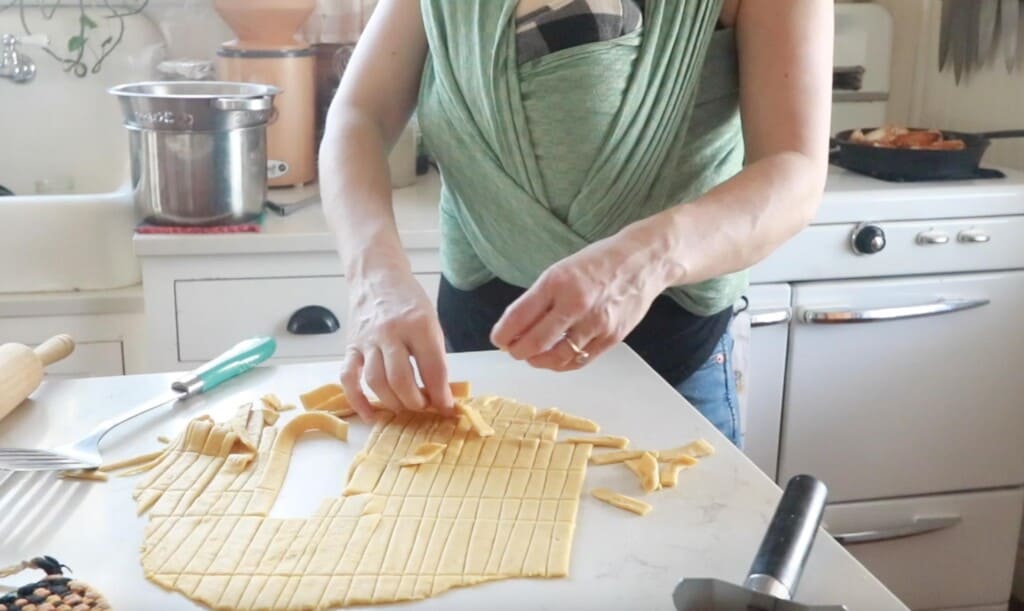 women pulling sliced noodle dough off of a white quartz countertop to place into soup.