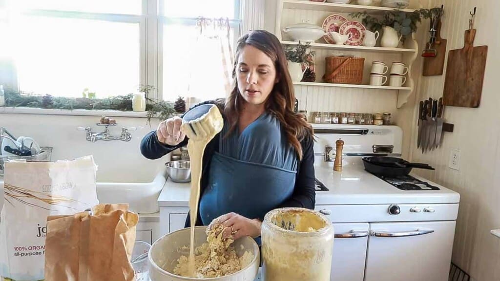 woman adding sourdough starter to a bowl of einkorn flour, water, and salt in her white kitchen