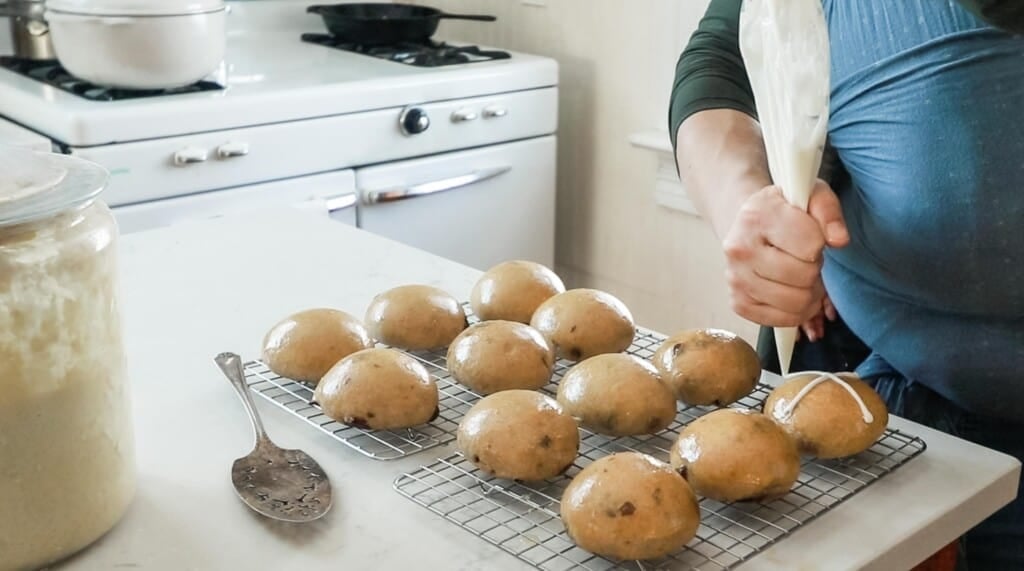 woman using a piping bag to pipe on a cross to sourdough hot cross buns pm