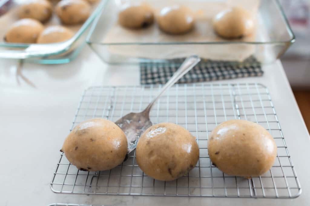 buns our of the oven on a wire rack cooking with glass baking pans in the background with more buns