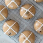 overhead photo of sourdough hot cross buns on a white rack on a quartz countertop