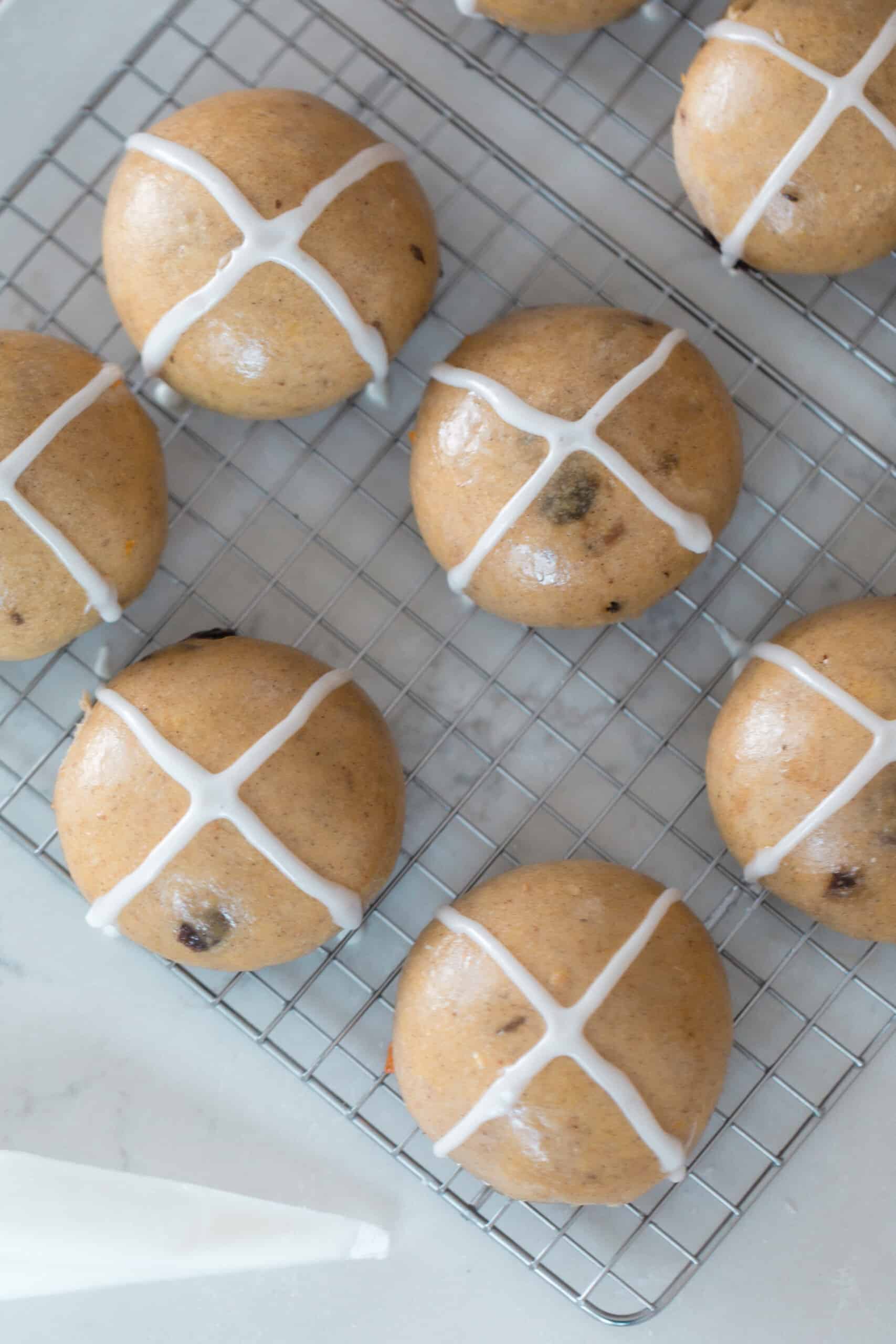 overhead photo of sourdough hot cross buns on a white rack on a quartz countertop