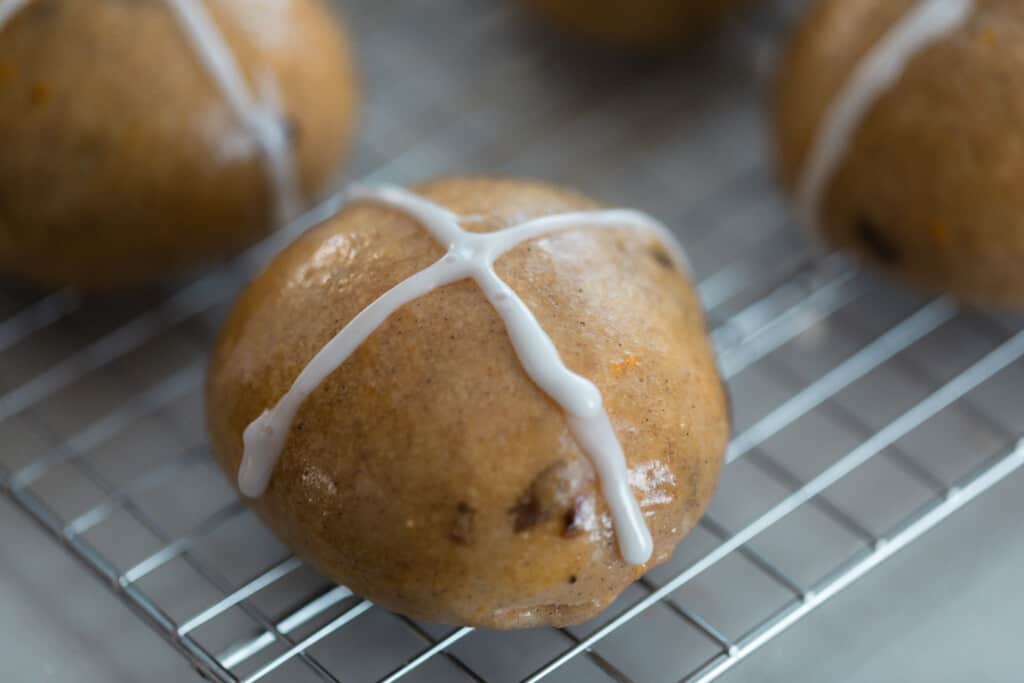 close up picture of a sourdough hot cross bun on a wire rack