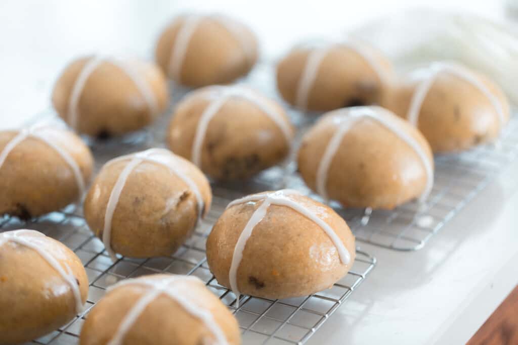 11 hot cross buns resting on a wire rack on a white quarts countertop