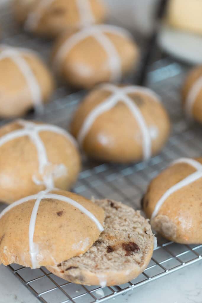 sourdough hot cross buns with an apricot glaze on a wire rack on a white countertop