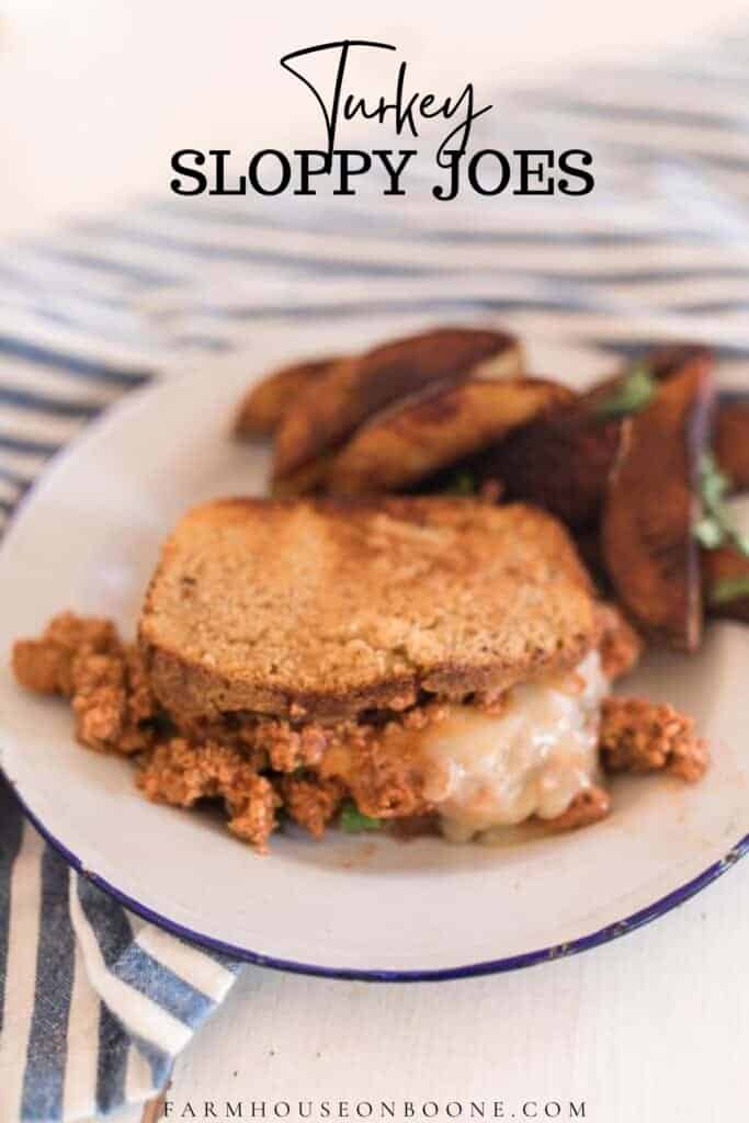 turkey sloppy joes covered in cheese on thick sliced sourdough bread with potato wedges on white plate with blue edges