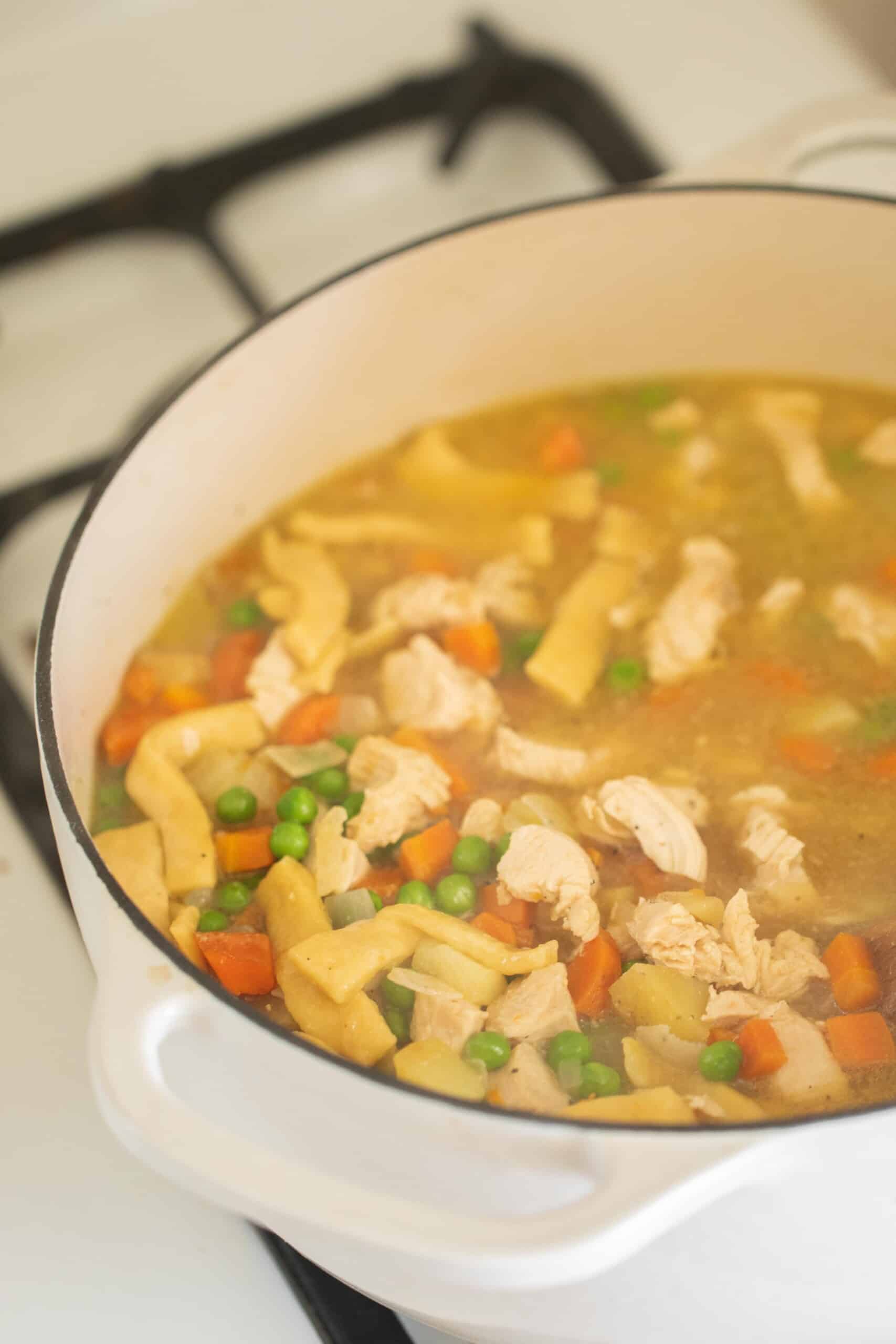 chicken noodle soup with homemade noodles in a white dutch oven on a white stove
