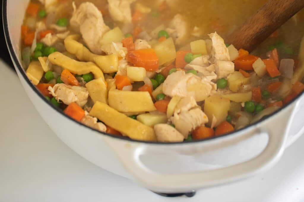 homemade chicken noodle soup with chicken, carrots, peas and homemade egg noodles in a dutch oven