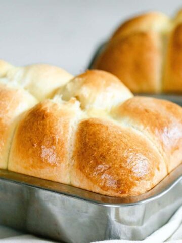 close up picture of delightfully fluffy and golden sourdough brioche in a stainless loaf pan and with another loaf in the background