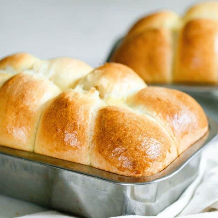 close up picture of delightfully fluffy and golden sourdough brioche in a stainless loaf pan and with another loaf in the background