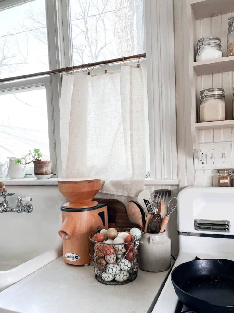 mockmill on a white countertop next to a basket of eggs and a vase full of utensils