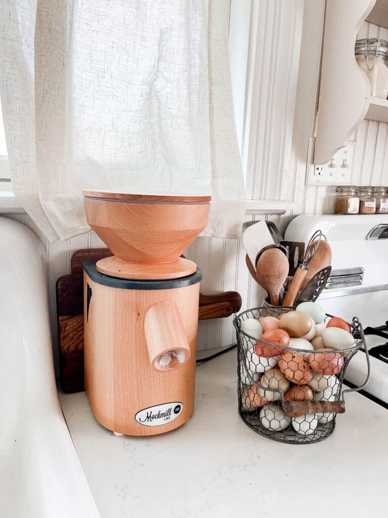 beechwood mockmill on a white countertop next to a basket of colorful farm fresh eggs