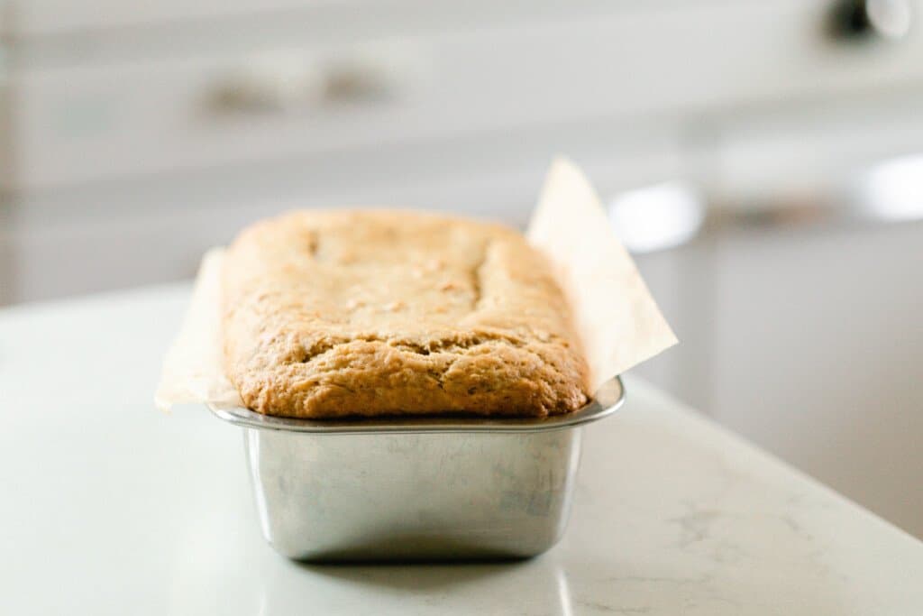 a loaf of sourdough banana bread in a stainless loaf pan on a white countertop