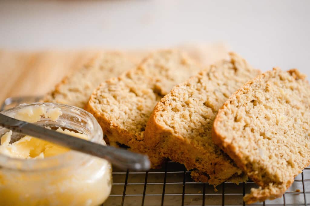 slices of sourdough banana bread on a wire rack with a jar of butter to the left